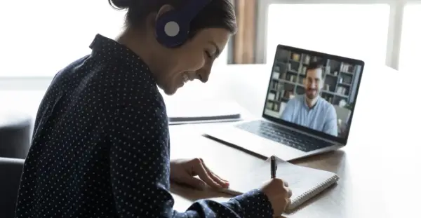Ragazza con cuffie sorride mentre prende appunti durante una lezione online, comprendendo il vero e-learning significato.